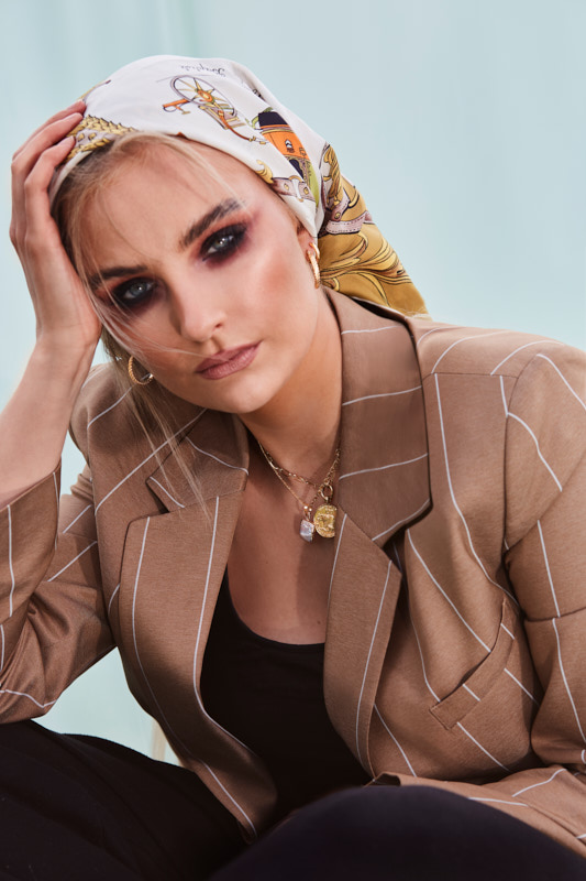Ein Close up Portrait für das Schmuck Label Necklays. Auf dem Bild zusehen ist eine junge Frau mit beigem Blazer und einem Tuch im Haar.